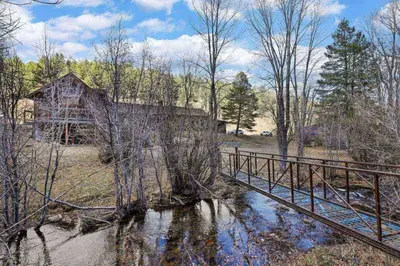 a bridge over a stream in front of a house at Cabin by North Clear Creek. Private Hot Tub. Pets in Black Hawk