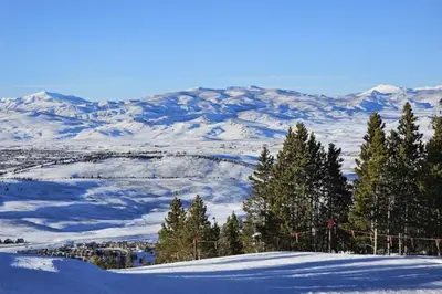 a snow covered hill with trees and mountains in the background at Mountainside 049 in Granby