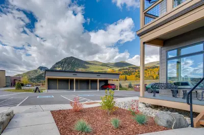 a building with a parking lot with mountains in the background at Walk to Ski Shuttles and Stores! Modern Frisco Unit in Frisco