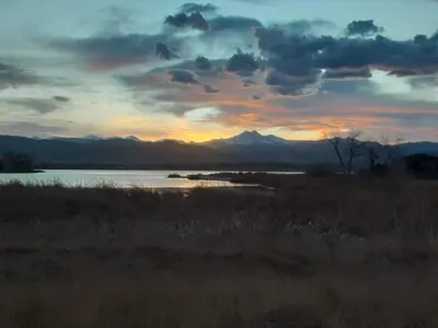 a sunset over a lake with mountains in the background at Steps to Lake Mcintosh, Basement 1BR in Longmont