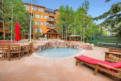 a patio with a pool with a waterfall and tables and benches at The Springs at River Run - Walk to Lifts, Pool Hot Tubs in Keystone