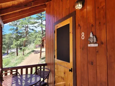 a door to a porch with two chairs and a table at Cabin 8-Cozy King Loft Cabin 5 Min to RMNP in Estes Park