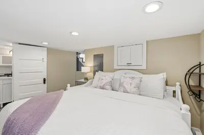 a bedroom with a large white bed and a kitchen at Kanons Kottage Downtown Retreat Near RMNP in Loveland
