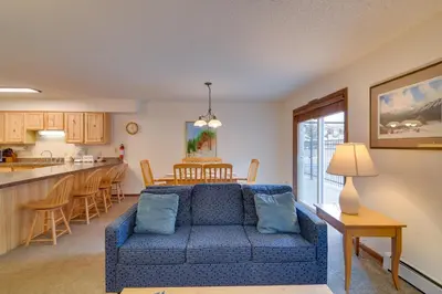 a living room with a blue couch and a kitchen at Ski, Soak and Chill! Pool-View Winter Park Condo in Winter Park
