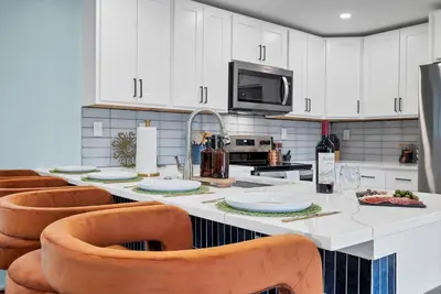 a kitchen with a large white counter with orange chairs at Outdoor Movie - Pingpong & Volleyball - Cozy 5BD in Denver