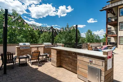 a patio with a grill and a bar with chairs at Fraser Crossing 1BR Condo | Hot Tub Access + Walk to Lifts in Winter Park