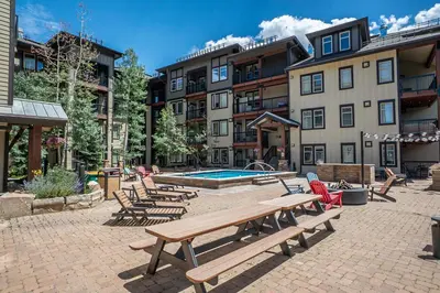 a patio with benches and a pool and buildings at Fraser Crossing 1BR Condo | Hot Tub Access + Walk to Lifts in Winter Park