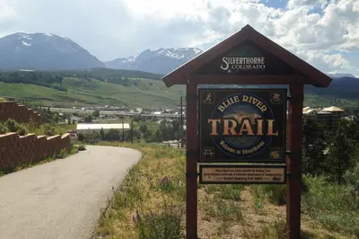 a sign for a trail with mountains in the background at 4th Street Alpine Loft - New - Central Ski Hub - King Bed, Garage Parking, Hot Tub, Great Location in Silverthorne