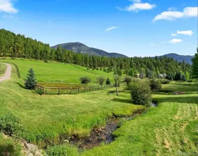a field with a fence next to a river at Modern barn by the creek in Evergreen