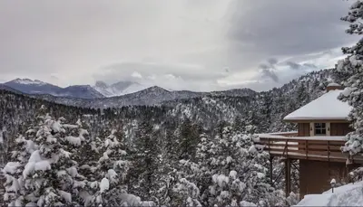 a cabin with snow covered trees and mountains at Rocky Mountain Panorama Cabin in Estes Park