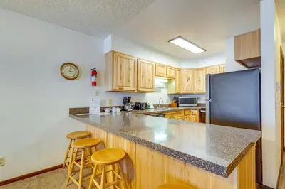 a kitchen with wooden cabinets and a black refrigerator at Heated Pool Access at Winter Park Base Camp! in Winter Park
