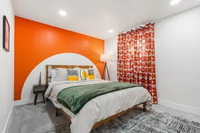 a bedroom with a bed with an orange wall at NEW Olde Town Arvada 5BR Luxe Mini Golf Hot Tub Arcade Cinema Gym in Arvada