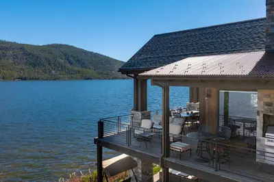 a house with a deck next to a body of water at LP Lakefront House - Private Dock, 7000+ Square Feet of Space, Stunning Views, Impeccable Quality in Grand Lake