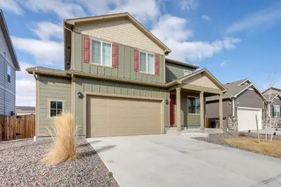 a green house with a garage at Work and Play! Denver-Area Home with Fenced Backyard in Fort Lupton