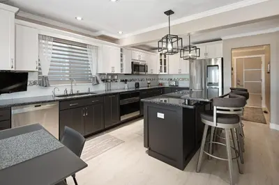 a kitchen with white cabinets and a black island with bar stools at Mountain View Modern Oasis - Swim Spa -Steam -More in Broomfield