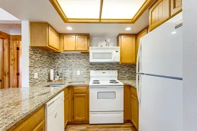 a kitchen with white appliances and wooden cabinets at Inviting and Cozy Fraser Condo Steps to Ski Shuttle in Fraser