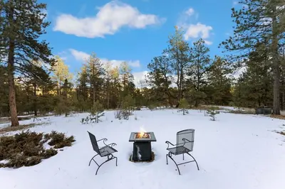 two chairs and a fire pit in the snow at The Pine Getaway on 60 Acres with Hot Tub in Pine