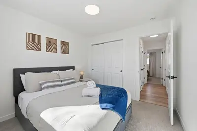 a white bedroom with a large bed and a hallway at Cozy 2BR Retreat with Backyard Lounge in Aurora
