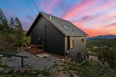 a black house with a sunset in the background at Family Mountain Getaway w Hot Tub and Amazing Views! Close to Hiking & Skiing in Idaho Springs