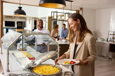 a woman holding a plate of food in a kitchen at Staybridge Suites Denver International Airport by IHG in Denver