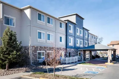 a large white building with a tree in front of it at Baymont by Wyndham Henderson-Northeast Denver in Henderson