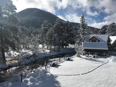 a house covered in snow next to a river at The Landing at Estes Park in Estes Park