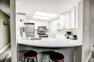 a kitchen with a white counter and two stools at Mountainside Trailview Condo: Cozy Frisco Retreat in Frisco