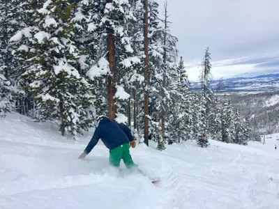 a person on a snowboard in the snow near trees at 4368 Founders Pointe Cozy WP Village Condo in Winter Park