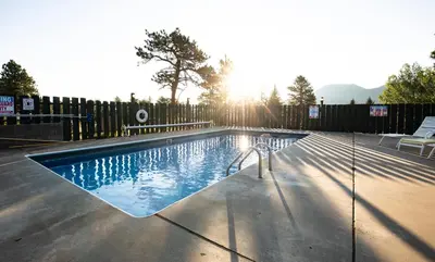 a swimming pool with the sun setting behind a fence at Saddle & Surrey Motel in Estes Park