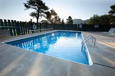 a swimming pool with blue water and a fence at Saddle & Surrey Motel in Estes Park