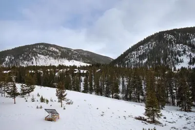a bench on a snowy hill with trees and mountains at 2092 The Pines Condo in Keystone