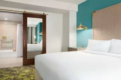 a bedroom with a large white bed and a bathroom at Embassy Suites By Hilton Boulder in Boulder