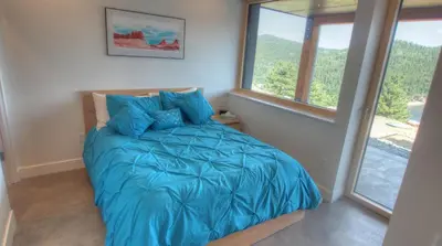a bedroom with a bed with blue sheets and windows at Timberline Haus Home in Nederland