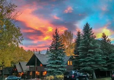 a house with pine trees in front of a sunset at Rams Horn Village Resort in Estes Park
