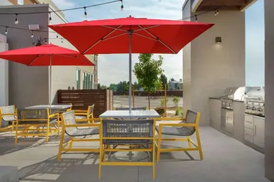 a patio with tables and chairs with red umbrellas at Home2 Suites By Hilton Longmont in Longmont