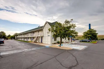 a large white building with a tree in a parking lot at Motel 6-Wheat Ridge, CO - West - Denver North in Wheat Ridge