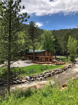 a log cabin in the woods next to a river at 4 Seasons Inn on Fall River in Estes Park