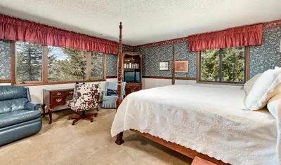 a bedroom with a bed and a chair and windows at Macmillan Home in Estes Park