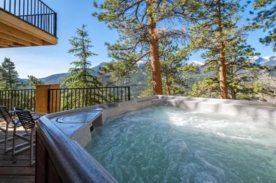 a hot tub on a deck with trees and mountains at Cedar Lower Condominium 2 Bedroom condo in Estes Park
