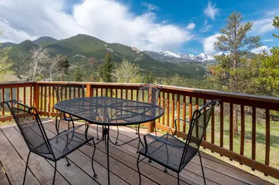a table and chairs on a deck with mountains at Salmans Bear Cove Home in Estes Park