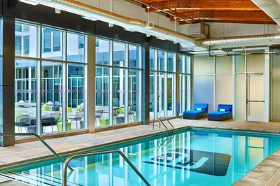 an indoor pool with blue chairs and windows at Aloft Denver Airport at Gateway Park in Aurora
