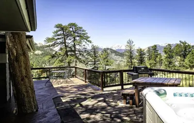 a deck with a table and a grill and mountains at Tranquil Duplex Home in Estes Park