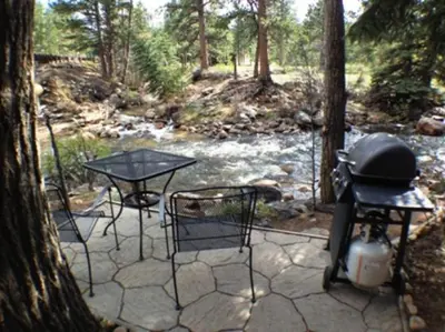 a grill and two tables and chairs next to a river at Swiftcurrent Lodge in Estes Park
