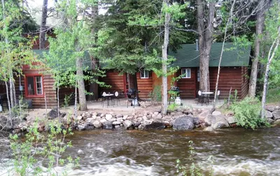 a log cabin with a river in front of it at Swiftcurrent Lodge in Estes Park