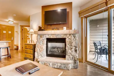 a living room with a stone fireplace with a flat screen tv at 1 Bedroom Colorado Vacation Rental In River Run Village Steps From The River Run Gondola in Keystone