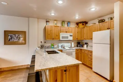 a kitchen with wooden cabinets and a white refrigerator at 1 Bedroom Colorado Vacation Rental In River Run Village Steps From The River Run Gondola in Keystone