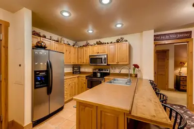 a kitchen with wooden cabinets and a stainless steel refrigerator at 2 Bedroom Colorado Vacation Rental In River Run Village With Pool And Hot Tub Access in Keystone