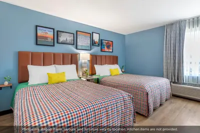 two beds in a room with blue walls and yellow pillows at Uptown Suites Extended Stay Denver CO -Westminster in Westminster