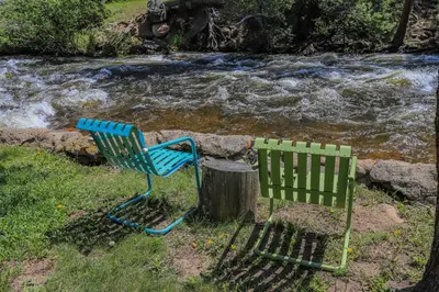 a green chair sitting next to a stump next to a river at Idlewilde by the River in Estes Park