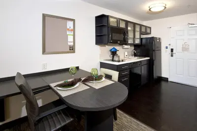 a kitchen with a dining room table and a kitchen with black cabinets at Candlewood Suites Greeley by IHG in Greeley